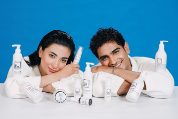 Two Pakistani models in white robes posing with a full range of Dr. Elements skincare and haircare products against a blue background