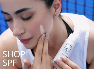 Model applying Dr. Elements SPF sunblock on her cheek while holding the product bottle