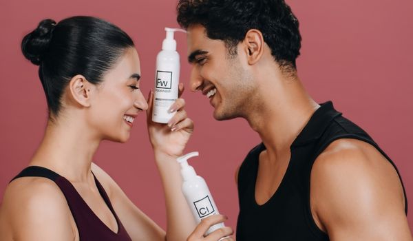 Two models smiling and holding Dr. Elements skincare bottles against a pink background
